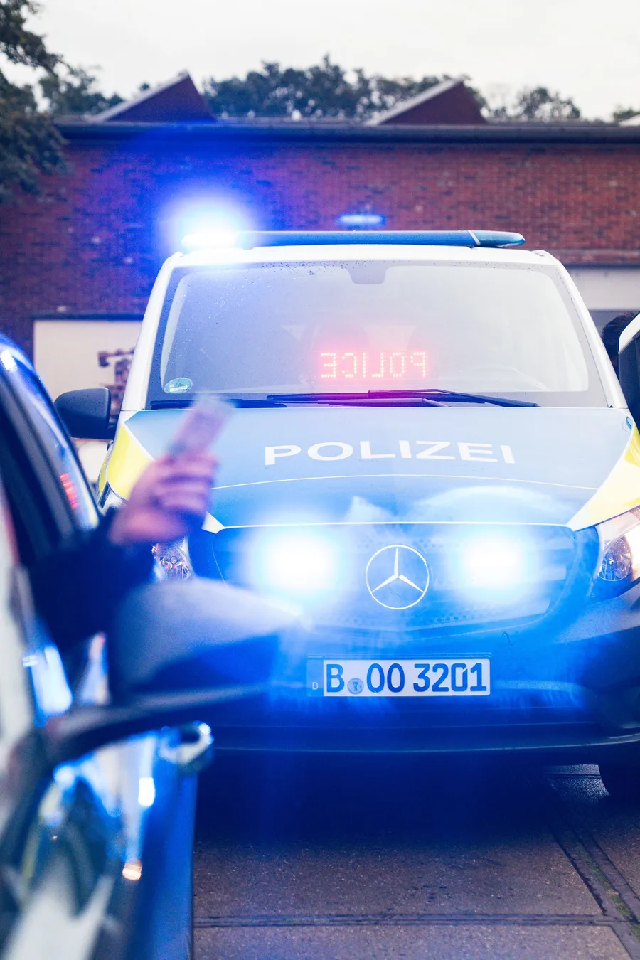 Eine Person wird von einem deutschen Polizeiauto angehalten. Blaulicht blinkt