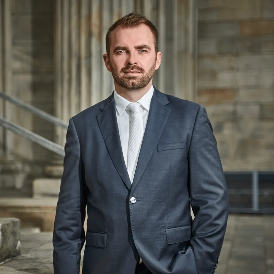 Mann im Anzug, Hände in den Taschen, steht vor einem Gebäude