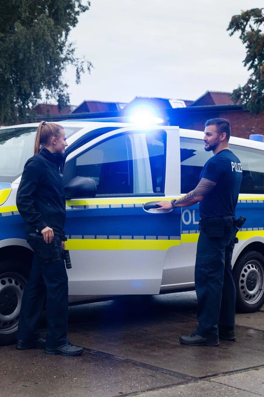Zwei Polizisten stehen neben einem Polizeiwagen mit Blaulicht